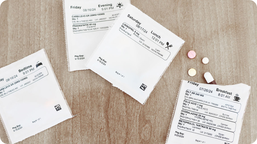 Four medication pouches with detailed labels on a wooden surface, accompanied by five various colored pills.