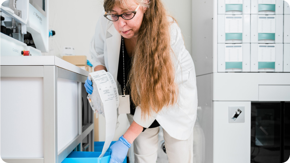 Woman in a lab coat working with a roll of labels in a laboratory.