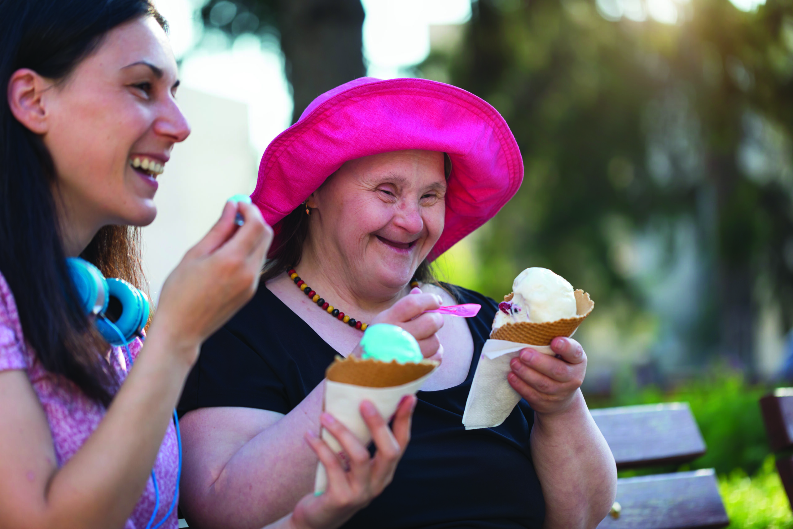 Woman with Down Syndrome and her friend eating ice cream and sitting on park bench
